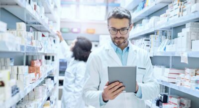Arzt in weißem Kittel liest auf einem Tablet, symbolisiert medizinische Beratung und Gesundheitsinformationen im Zusammenhang mit Apotheken und Medikamenten.